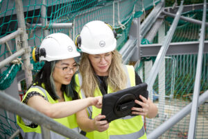 Two I&G workers in hard hats look at a tablet screen on a building site